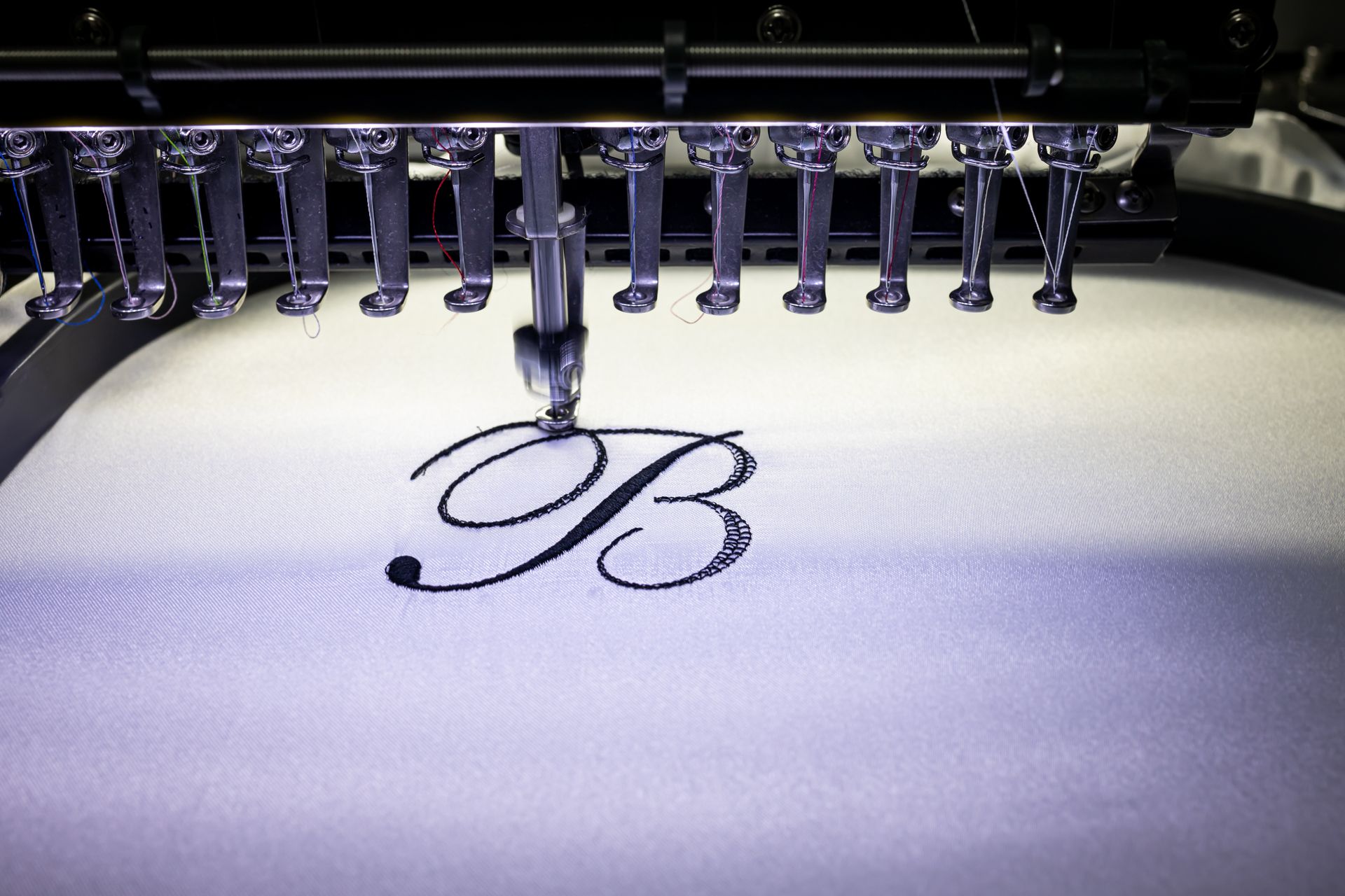 An industrial embroidery machine stitching a black script letter 