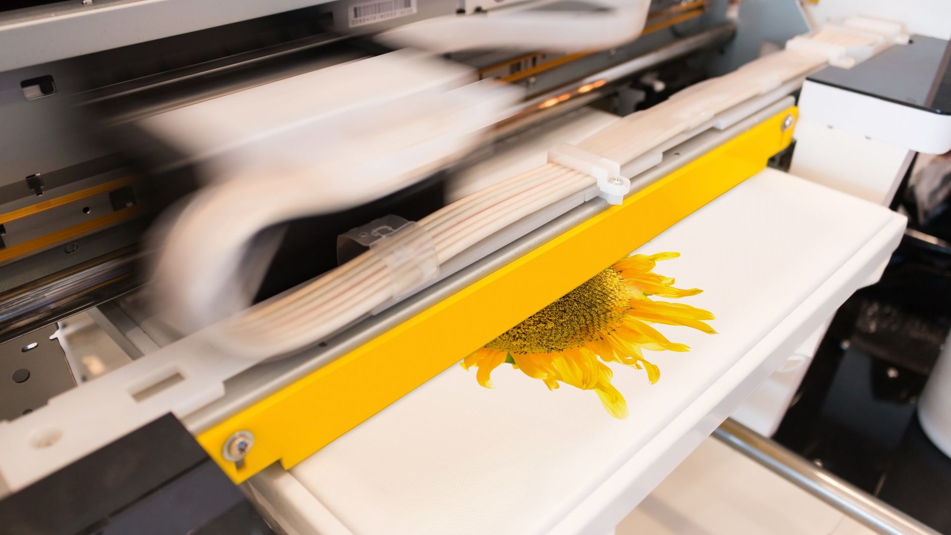 A digital printer prints a vibrant yellow sunflower onto a white textile surface.