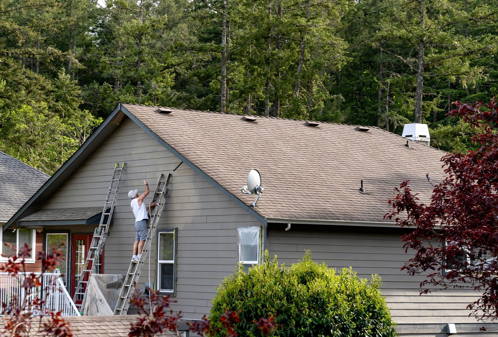 Workers on a gray house roof, repairing curled shingles with ladders and tools