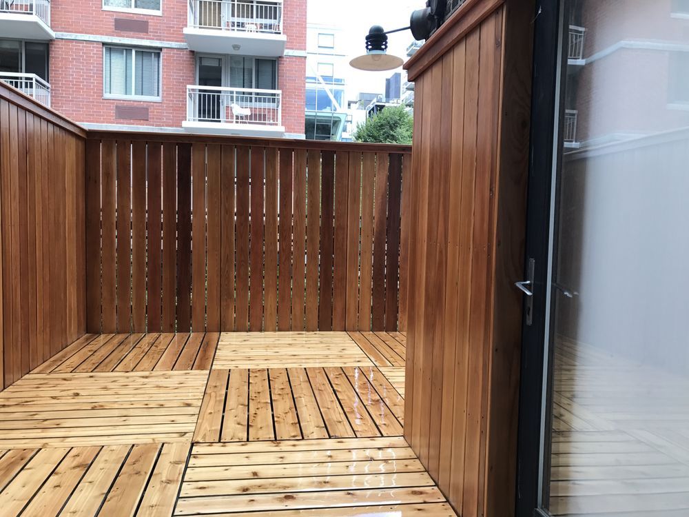 Wooden patio with a slatted fence, door, and a building in the background.