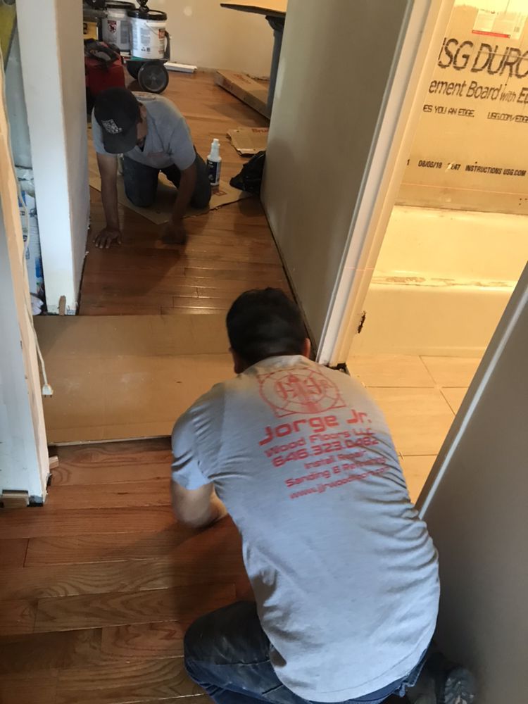 Two workers installing hardwood floor in a doorway. One kneels, the other is further away.