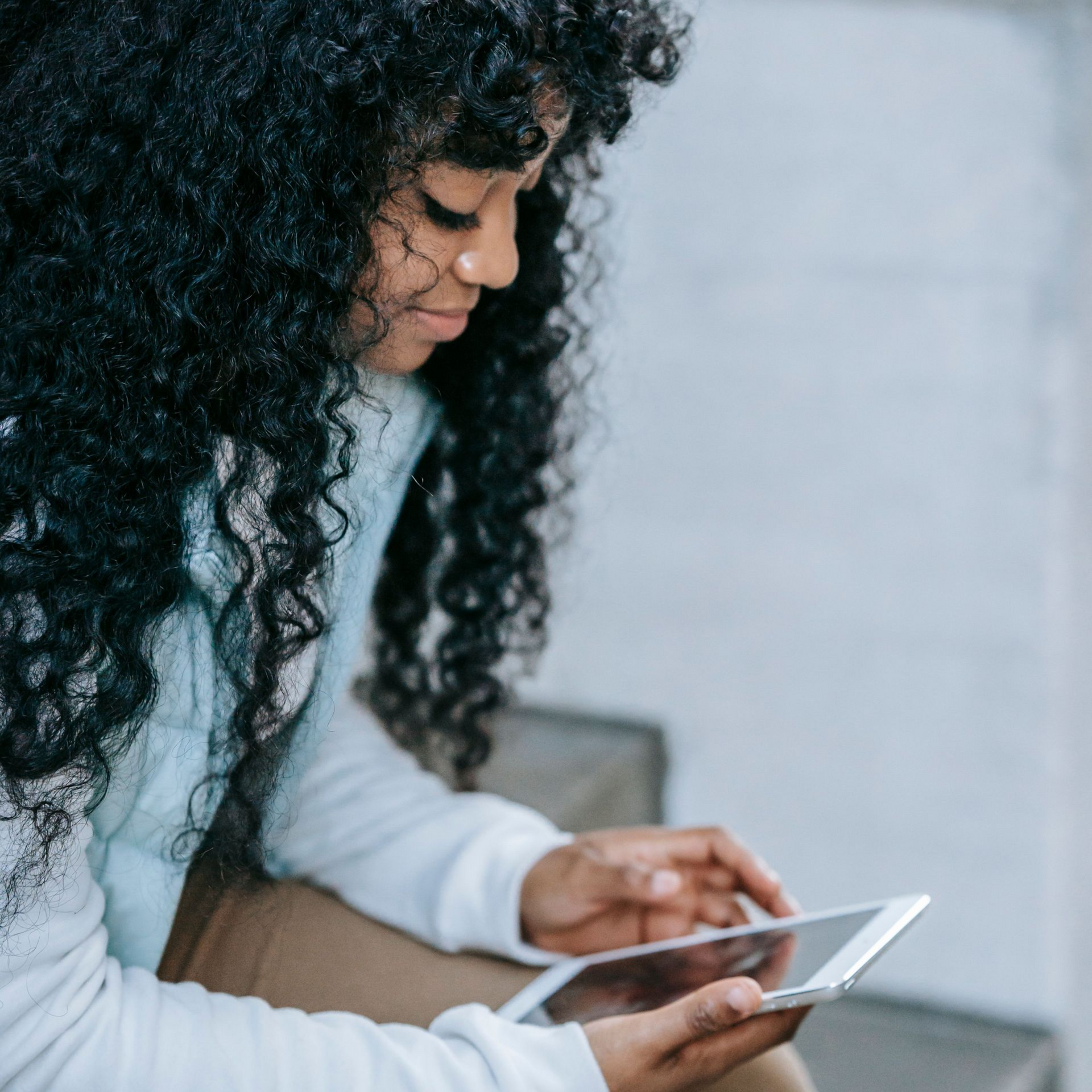 Person with curly hair looking at a tablet while sitting indoors
