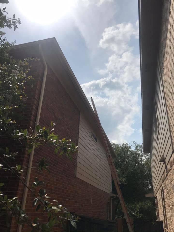 Narrow alley between brick buildings with a ladder leaning against the left wall under a bright sky.