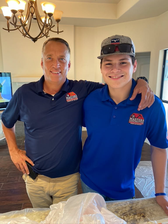 Two men in navy and blue polo shirts smiling together indoors by a table