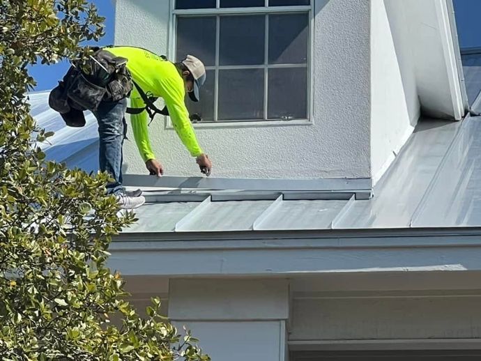 Worker in neon yellow gear repairing a metal roof beside a window.