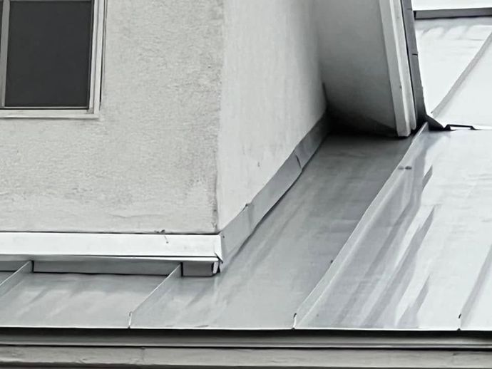 Roof with gray metal panels and a small window on a white building exterior