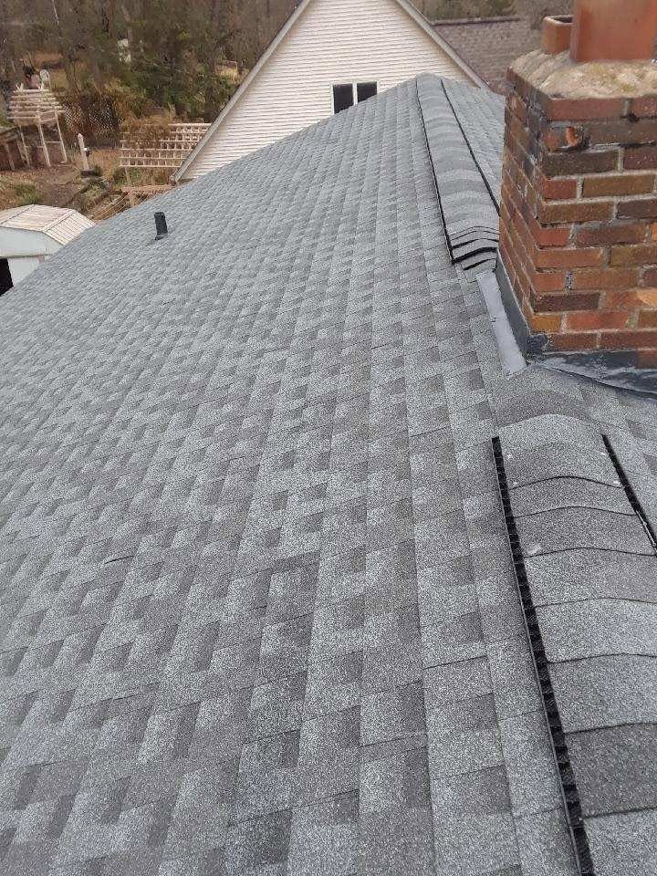 Gray shingled roof with a brick chimney and nearby house roofline