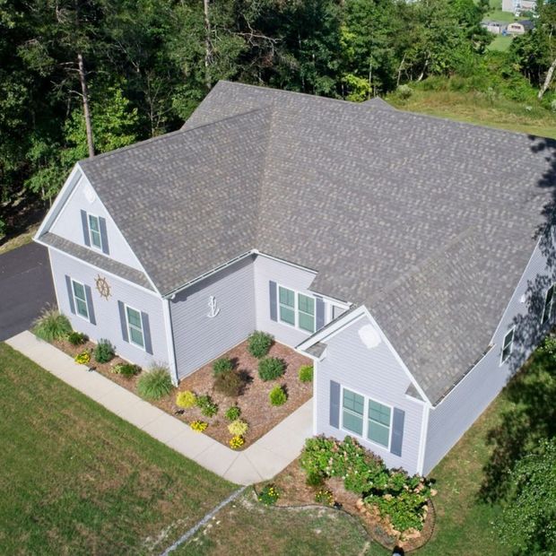 Aerial view of a gray-roofed white house with green shutters and a landscaped yard