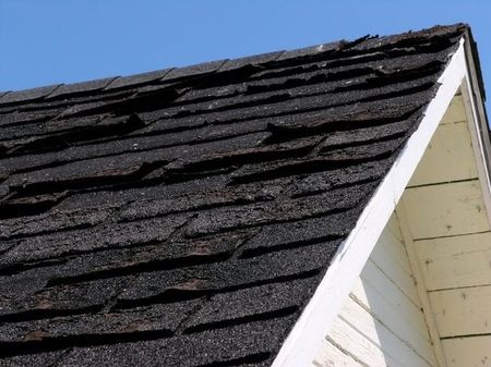 Close-up of a dark shingled roof against a blue sky, showing the white gable edge.