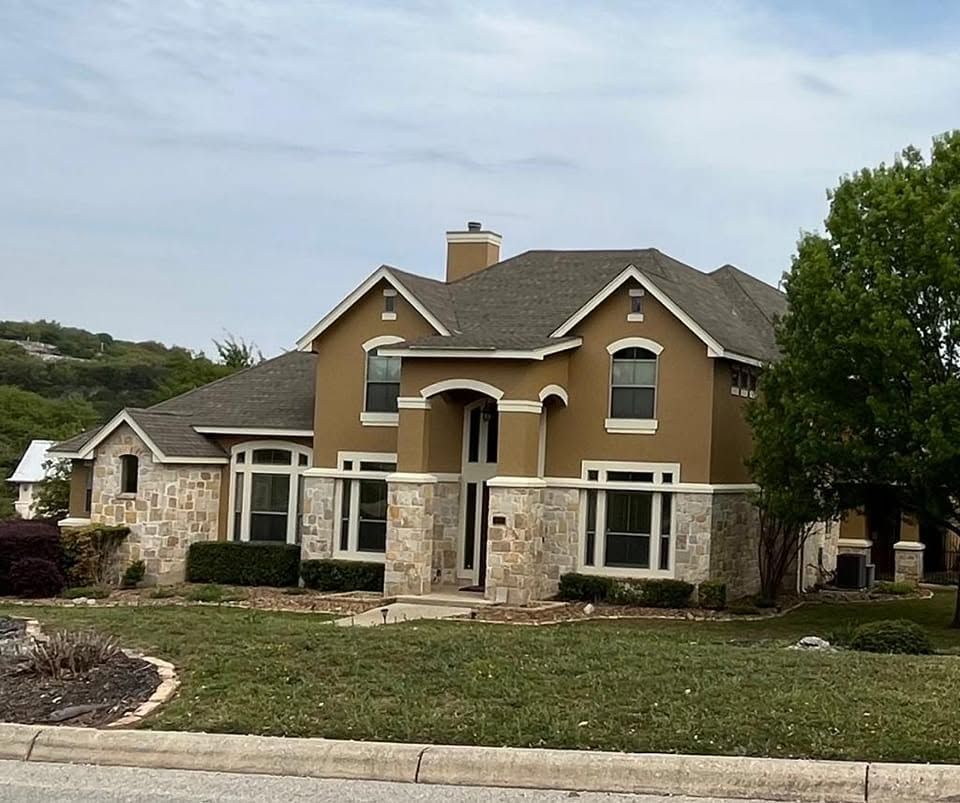 Large tan suburban house with stone facade, white trim, and a front lawn under cloudy skies
