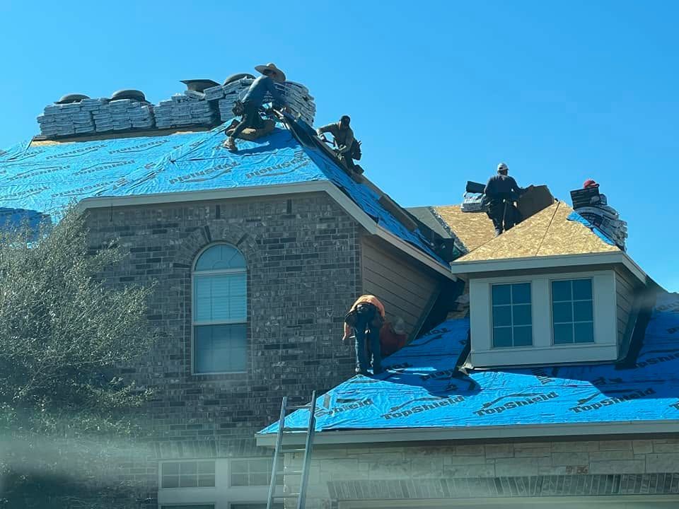 Roofers working on a house roof covered with blue tarps and shingles under a clear sky