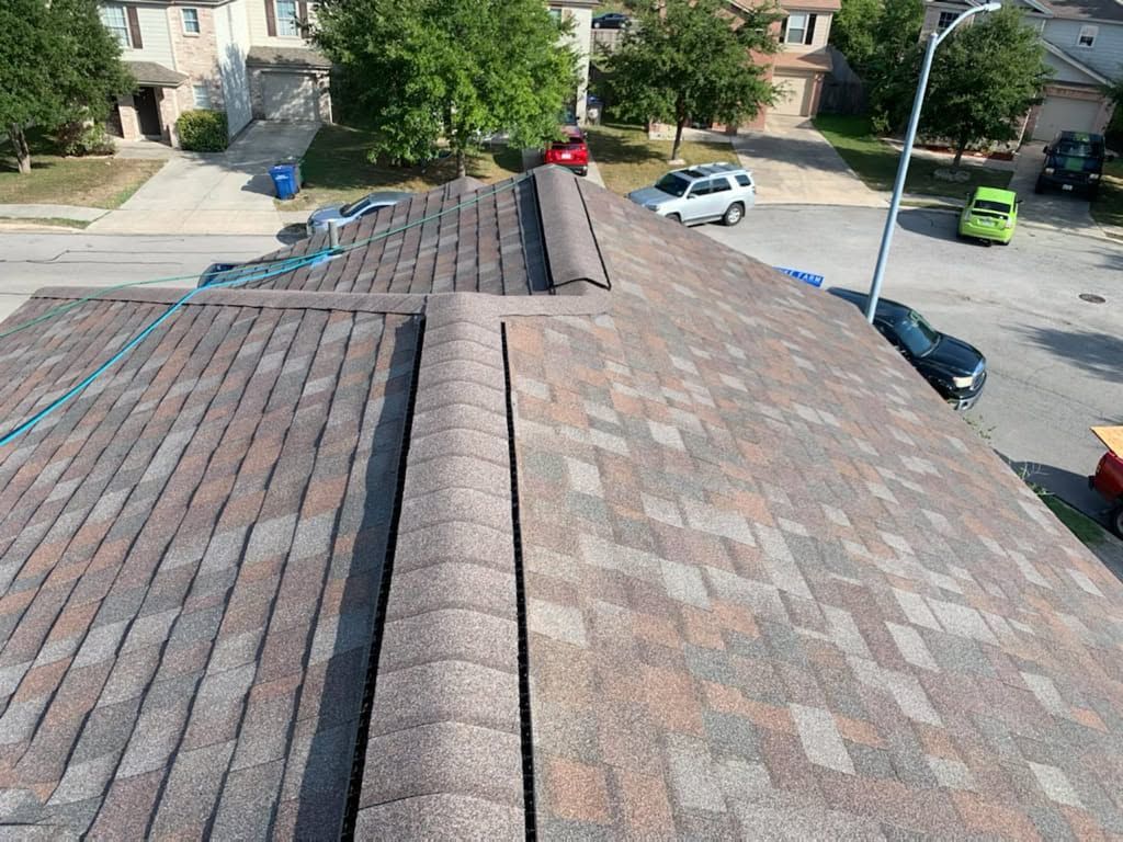 Rooftop with brick shingles and a central ridge, overlooking a quiet suburban street with parked cars.