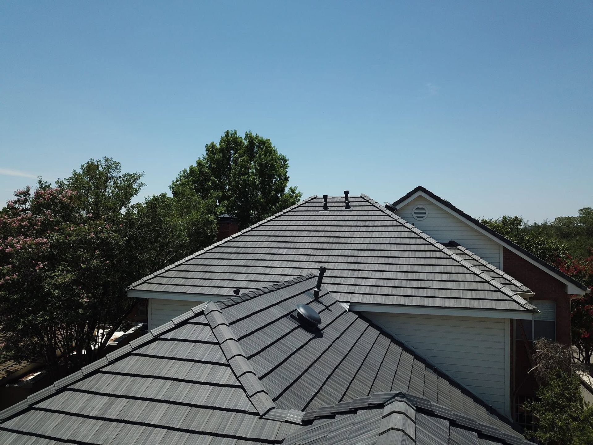 Residential rooftops with gray shingles under a clear blue sky, seen from above