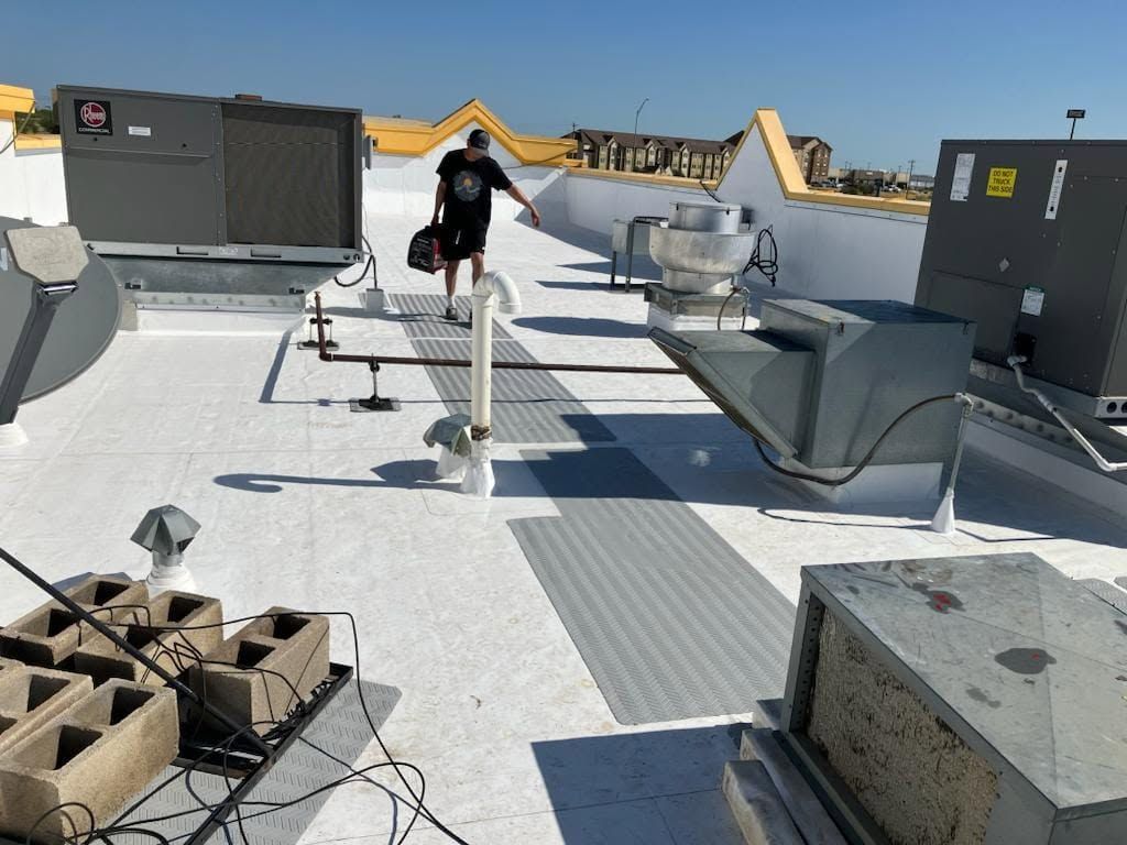 Rooftop with HVAC units, vents, and a worker walking along a white gravel path under a clear blue sky