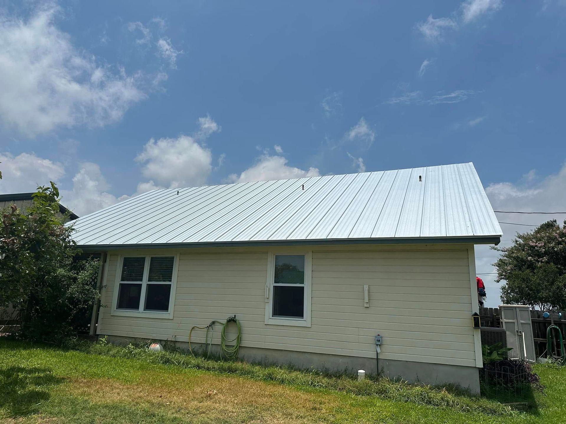 Single-story beige house with a white metal roof under a blue sky