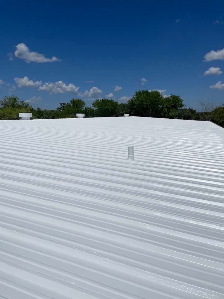 White corrugated roof under a blue sky with scattered clouds and trees in the distance