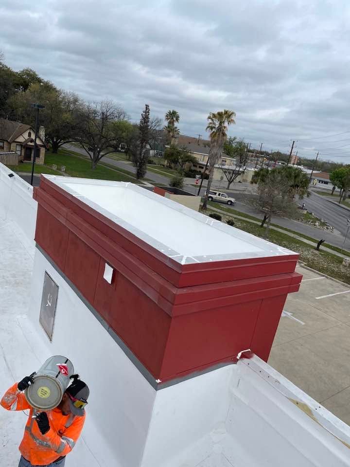 Worker in orange safety gear inspecting the rooftop of a red building under cloudy skies.