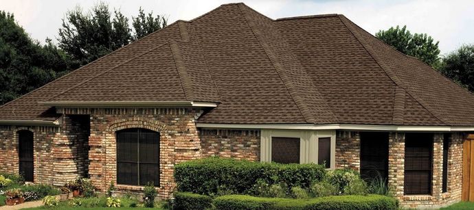 Brick house with a large brown shingle roof, front porch, and trimmed hedges