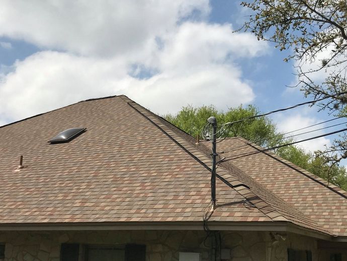Roof with brown shingles, skylight, and vent pipes beneath a cloudy sky