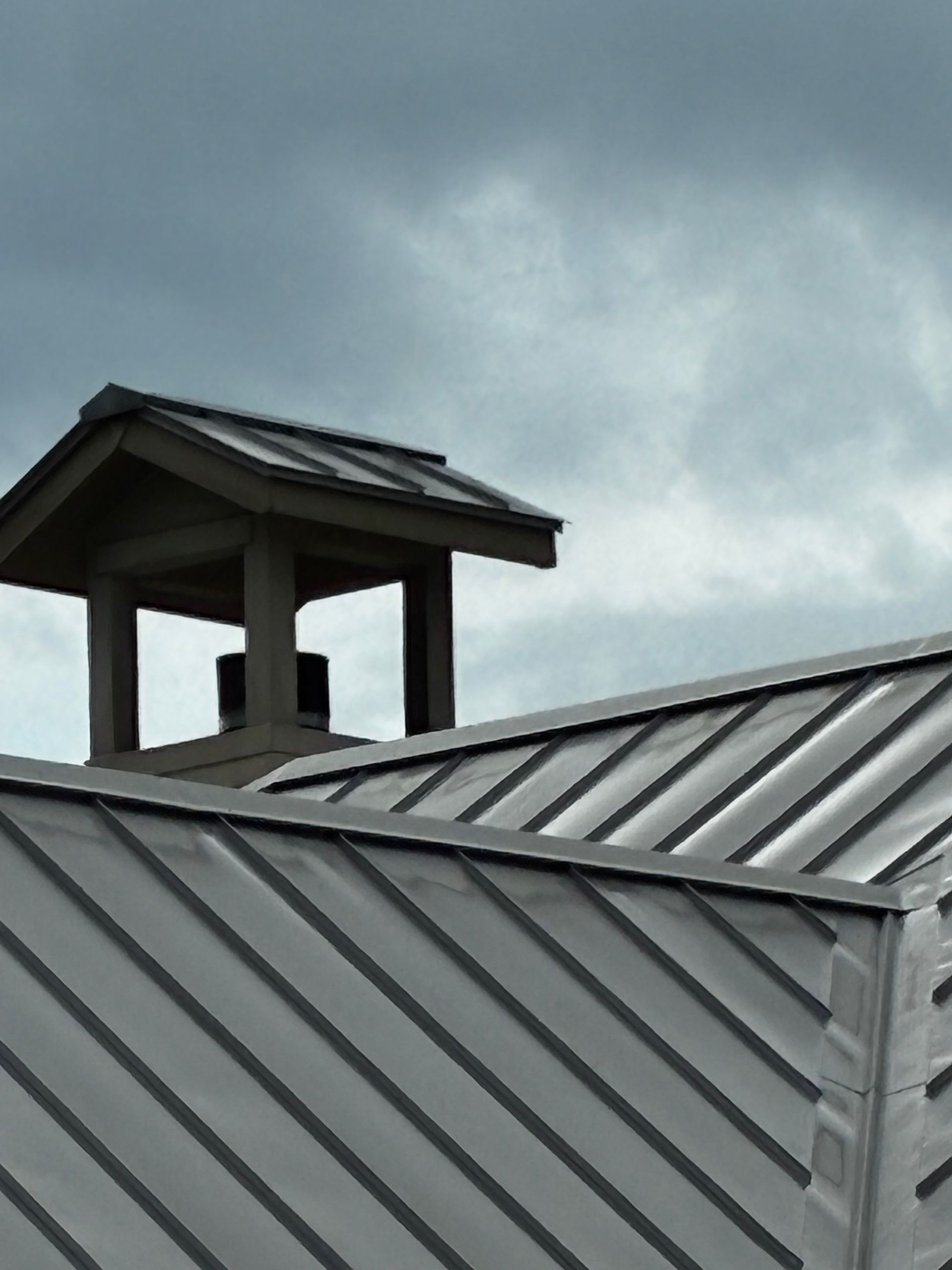 Gray metal rooftop with a small chimney under a cloudy sky