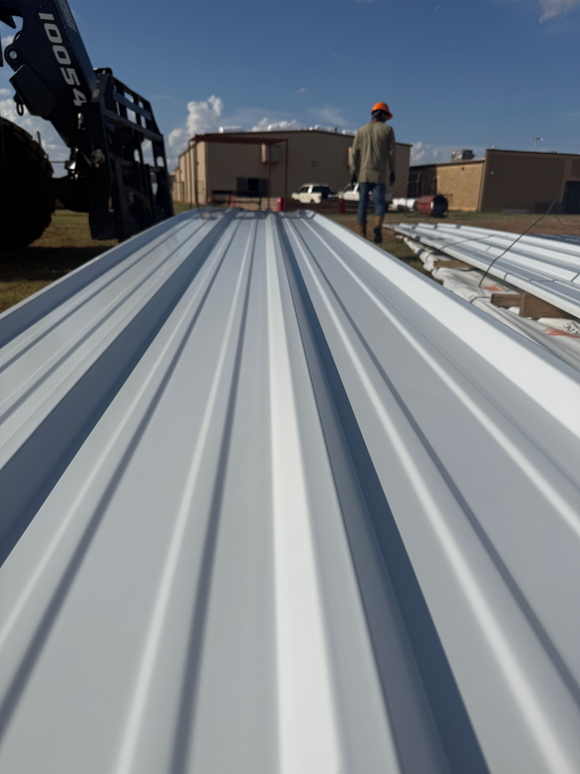 Worker on a corrugated metal roof at a construction site under a clear blue sky