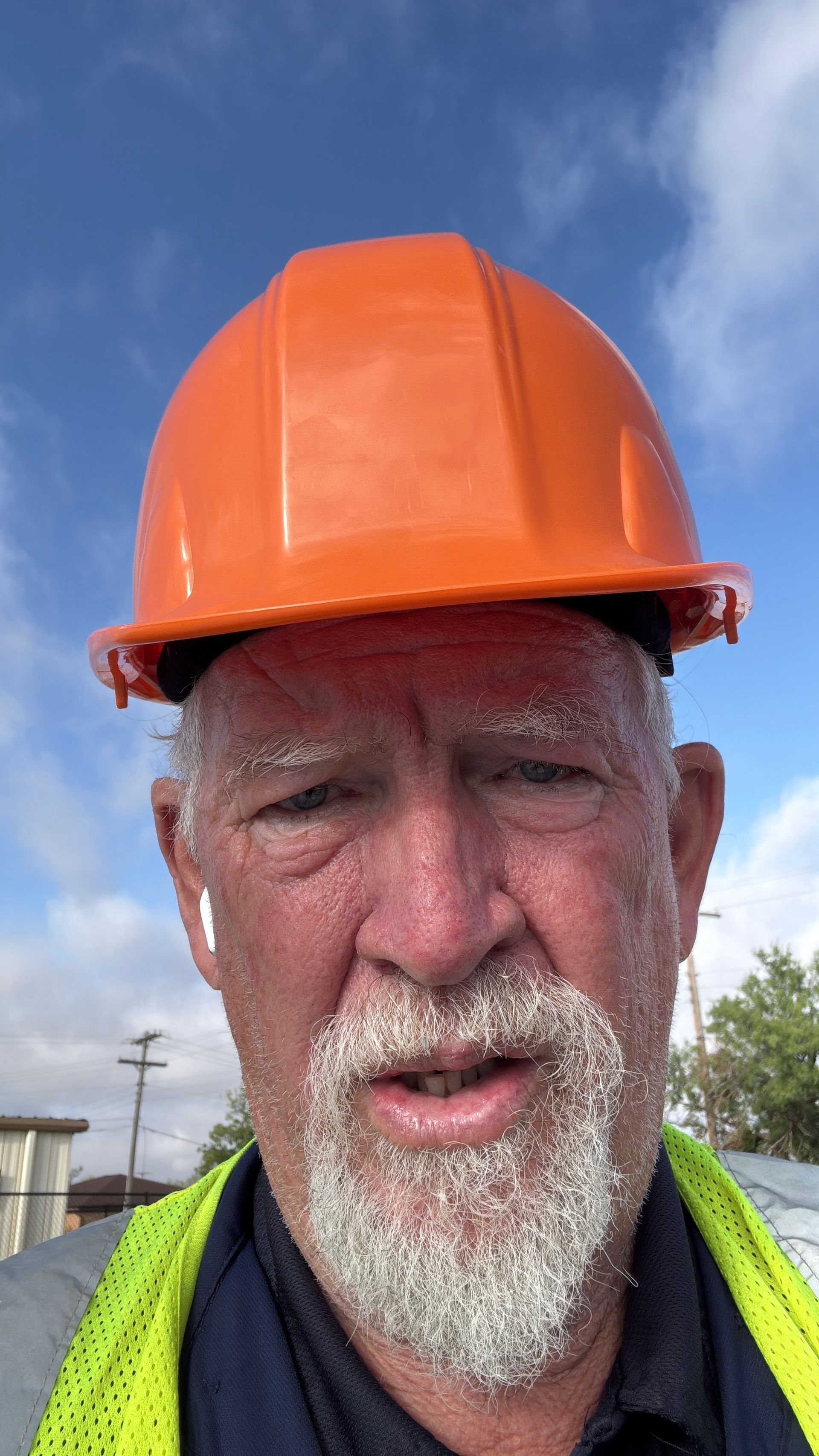 Close-up of a worker wearing an orange hard hat outdoors under a blue sky