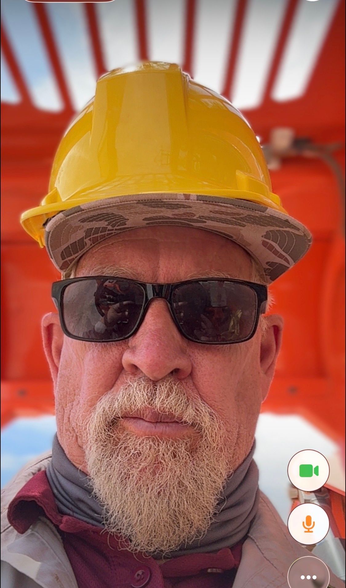 Man wearing a yellow hard hat and sunglasses in a red industrial setting