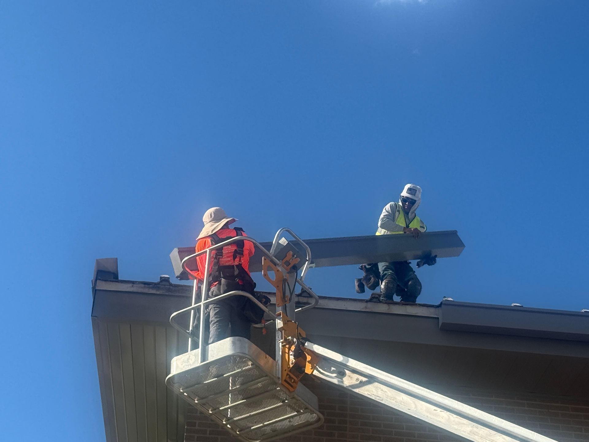 Workers on a rooftop using a lift platform to repair the roof under a clear blue sky