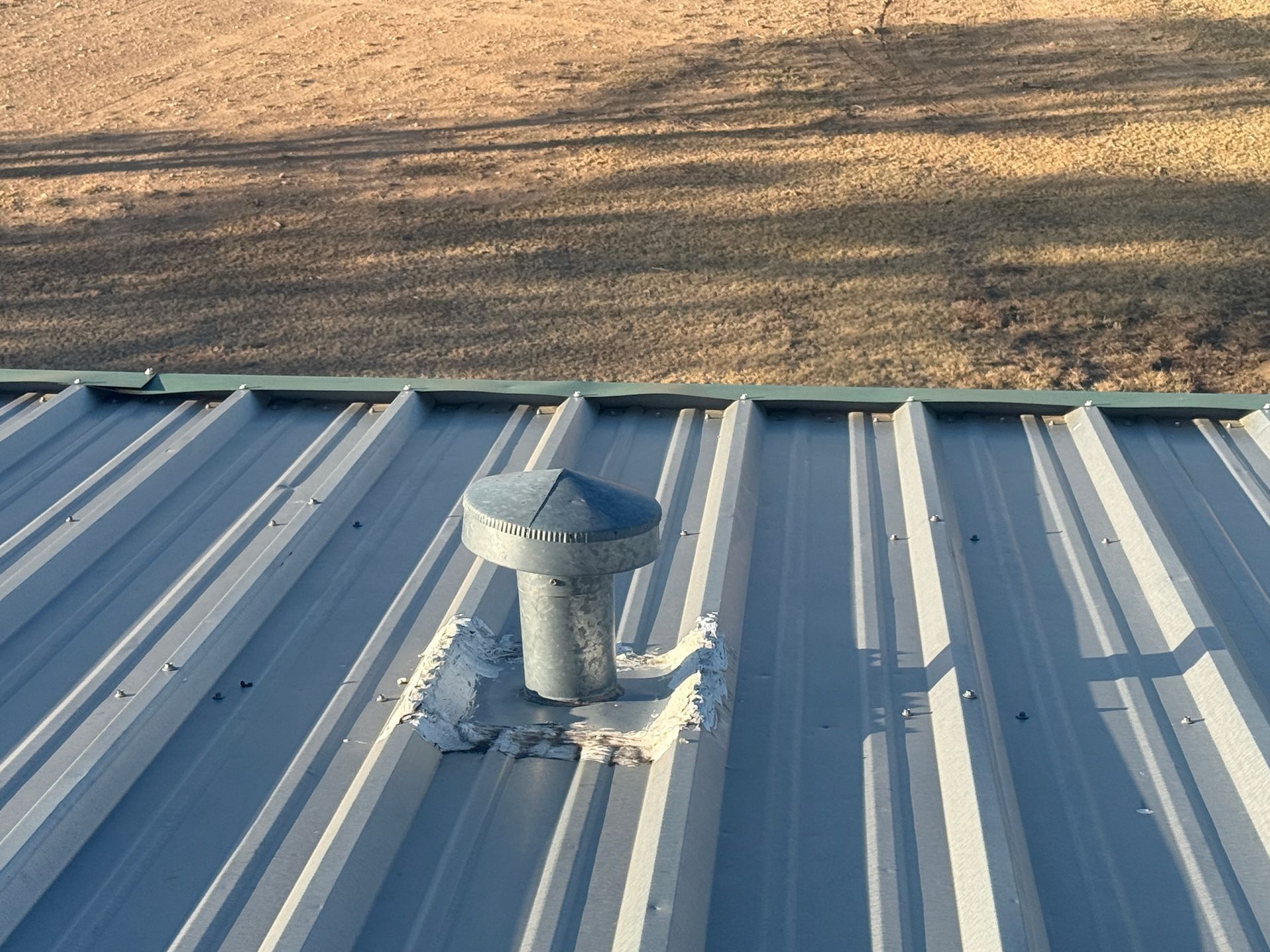 Metal roof vent on a corrugated gray rooftop with sunlit brown grass in the background