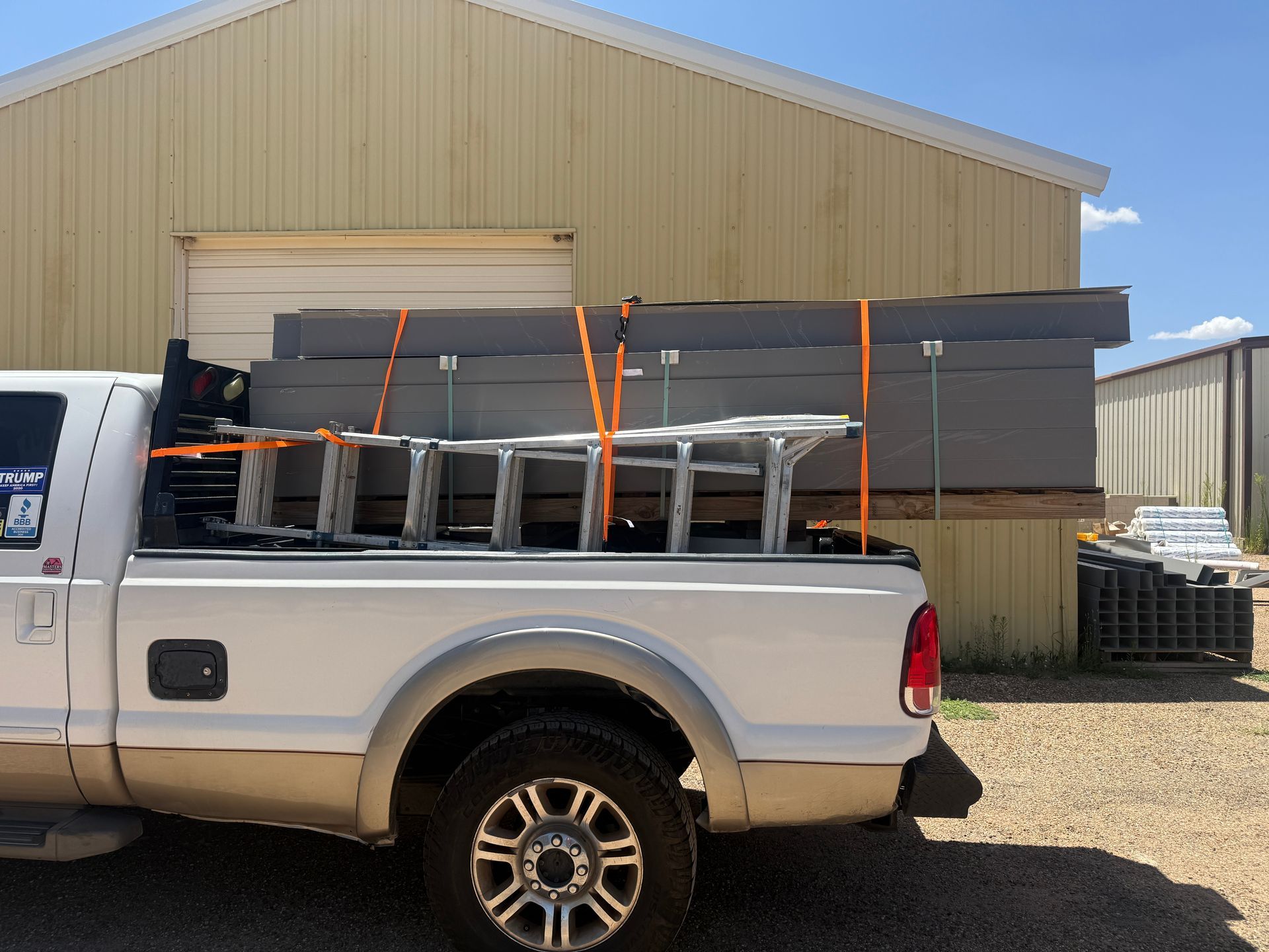 Silver pickup truck loaded with strapped black panels in front of a beige warehouse