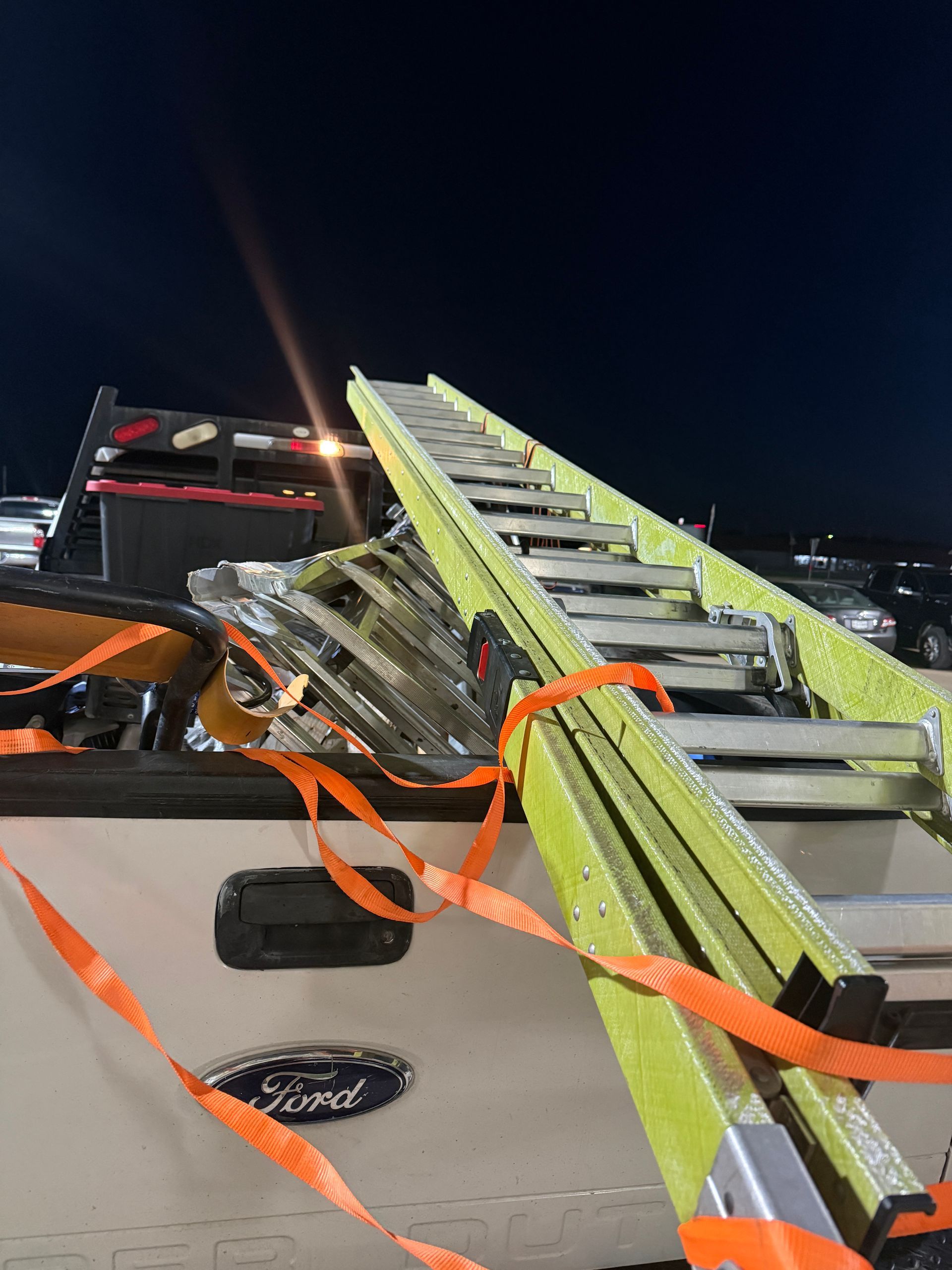 Fire truck ladder extended upward at night, with orange straps securing equipment on the truck bed