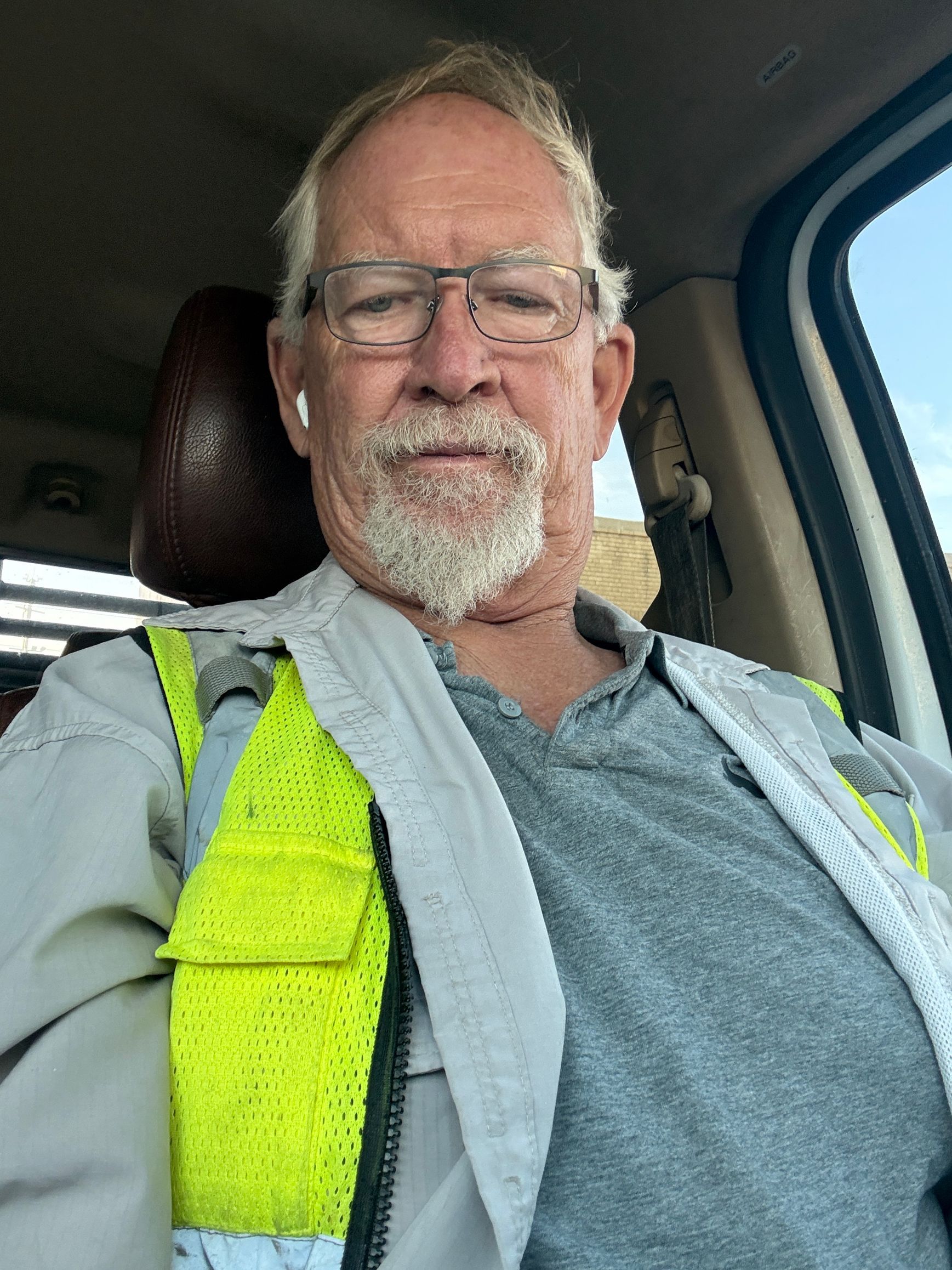 Man wearing safety vest and glasses sitting in a vehicle, looking at the camera.