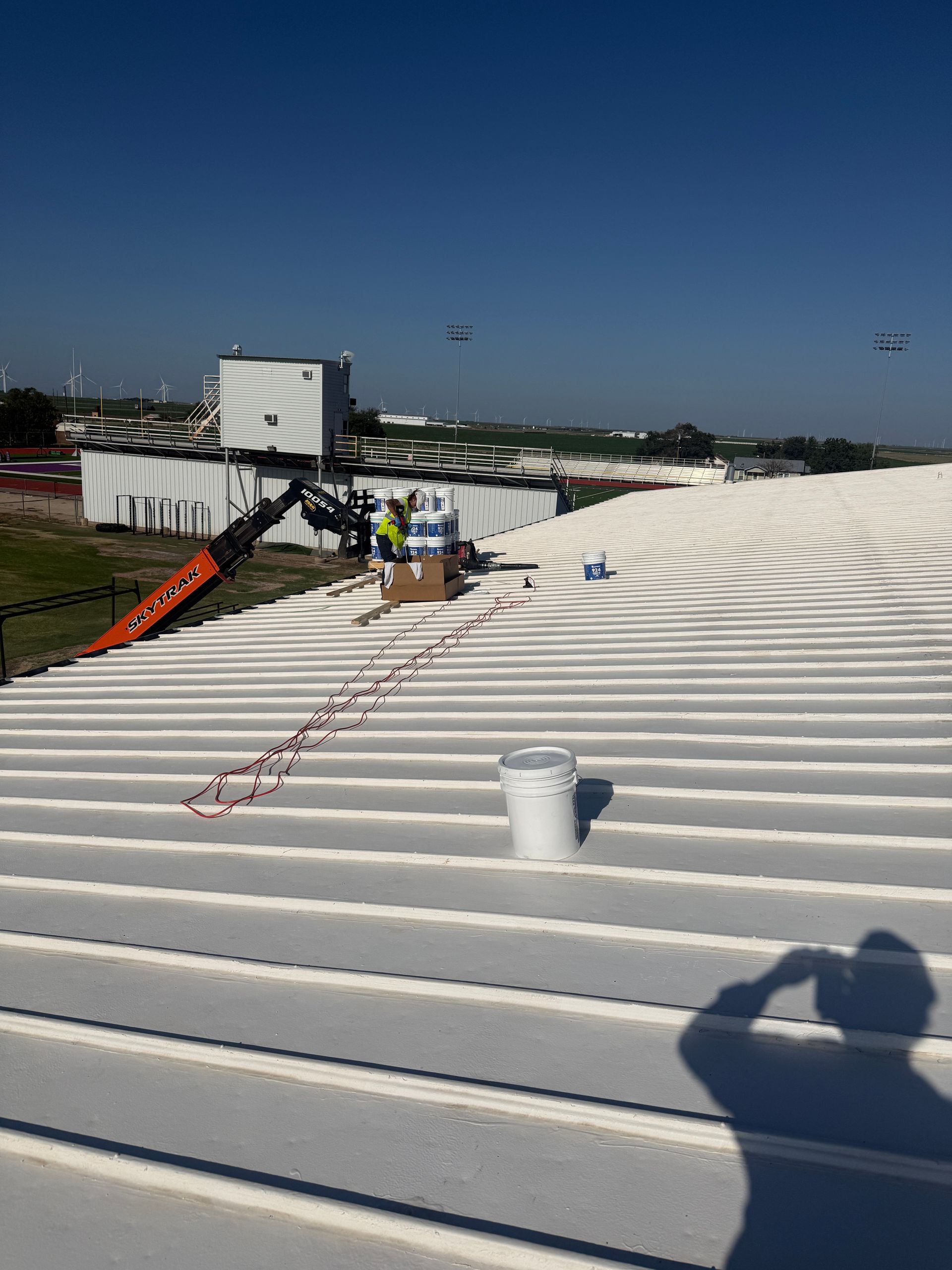 White corrugated rooftop under a clear blue sky with workers and equipment in the distance