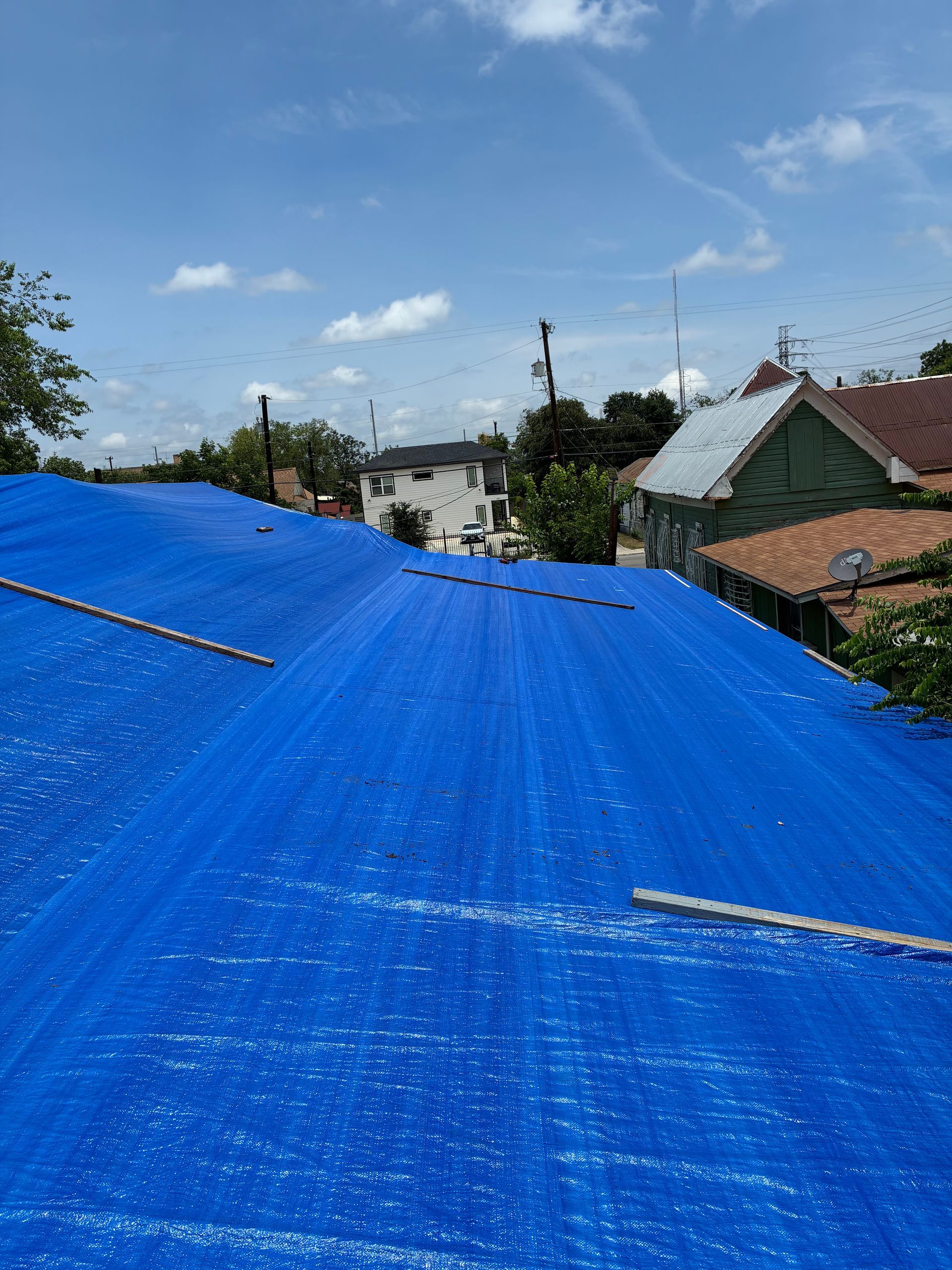 Blue tarp covering rooftops in a neighborhood under a clear sky