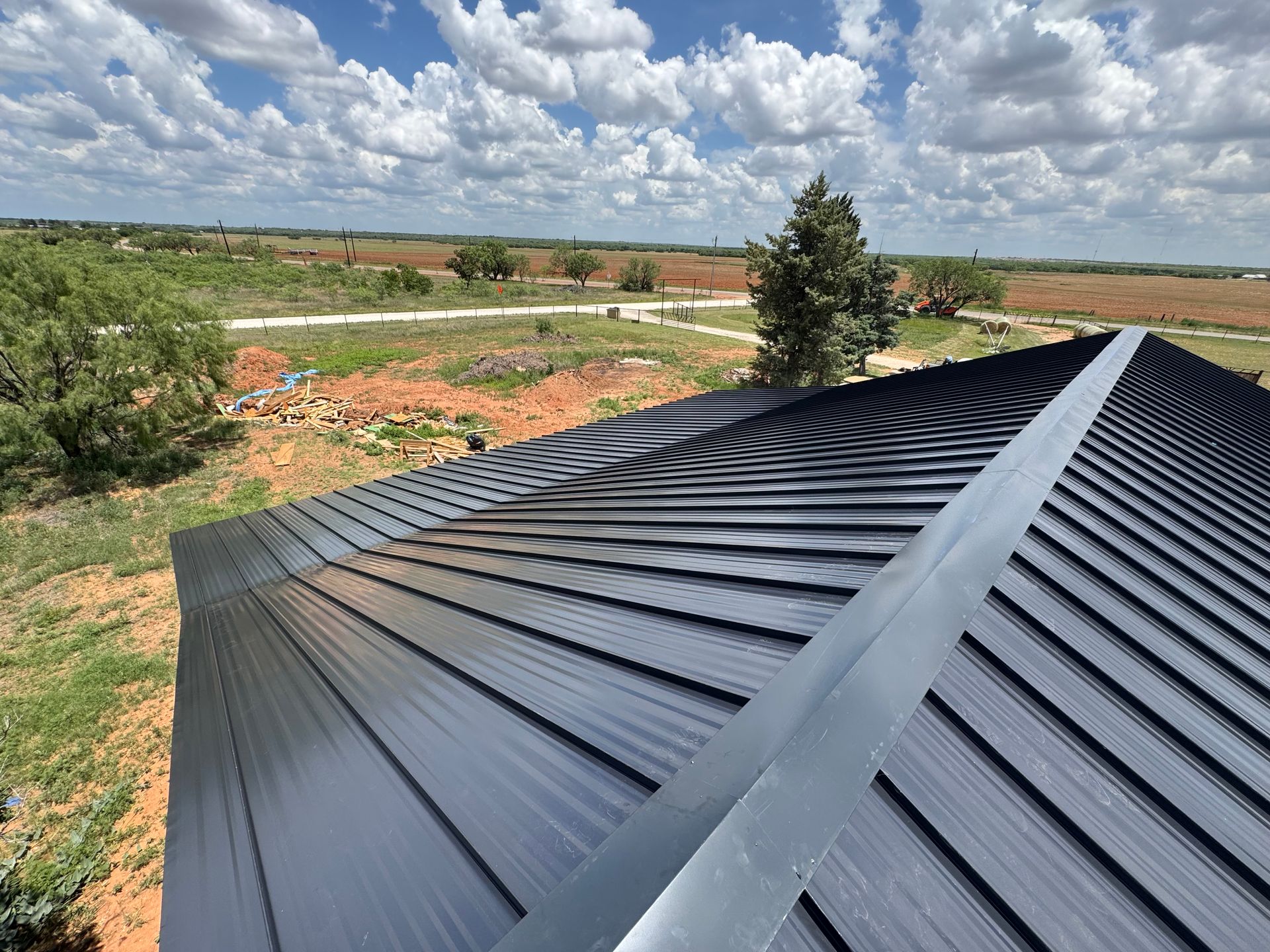 Black metal roof under construction overlooking a rural landscape with clouds overhead