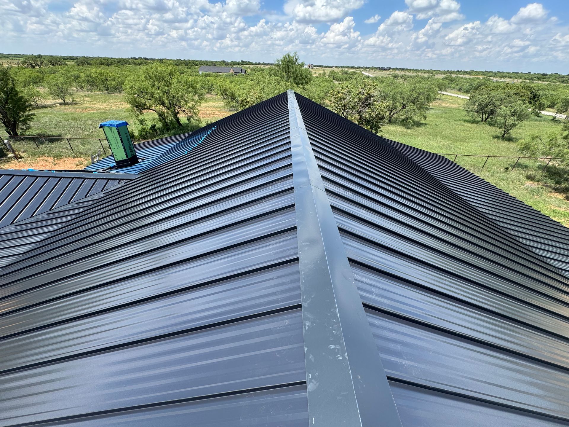 Black metal roof with a central ridge, overlooking green fields and a partly cloudy sky