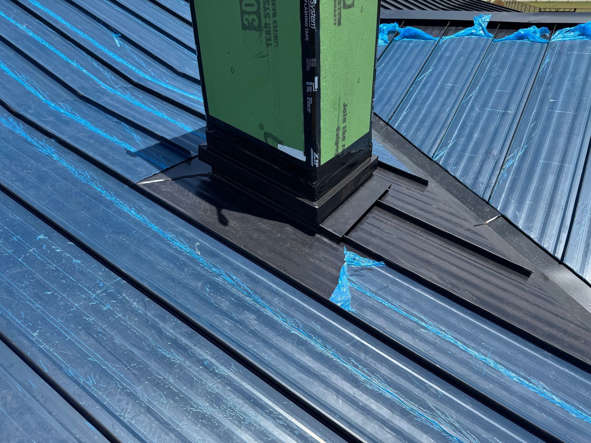 Green chimney pipe on a blue corrugated metal roof with black flashing.