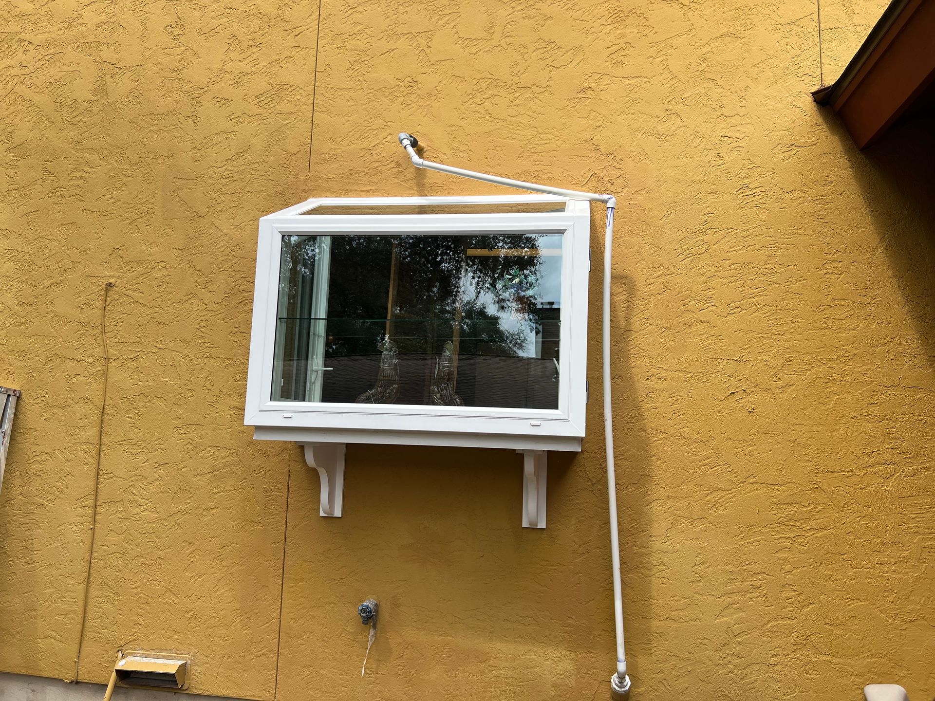 White window air conditioner mounted on a yellow stucco wall with a white conduit pipe nearby