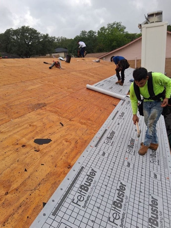 Workers installing roofing underlayment on a sloped orange roof on an overcast day