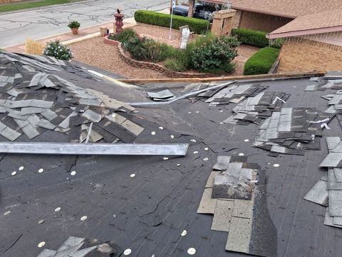 Damaged shingle roof with missing sections after a storm, overlooking a suburban street and houses