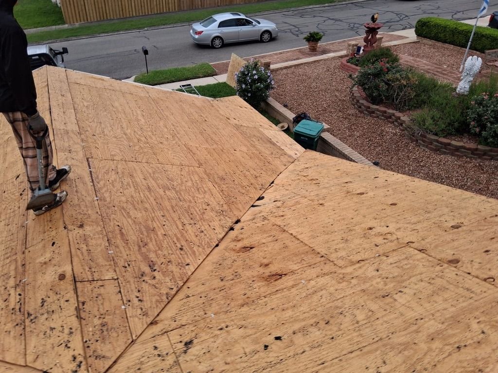 Roofers installing plywood sheathing on a house roof, with a street and parked car below.