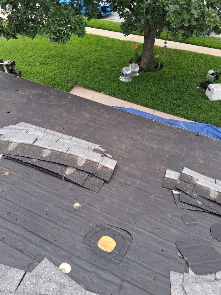 Damaged rooftop with scattered shingles, a tree and grassy yard below, and small outdoor lights along the edge