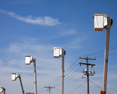 Tall utility poles with white equipment boxes and power lines against a clear blue sky.