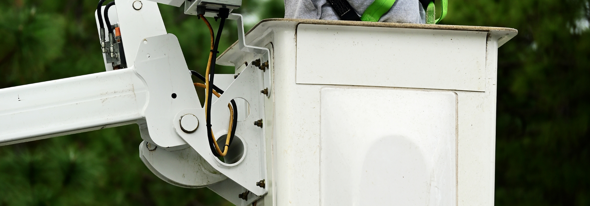 White utility bucket truck lift next to green foliage