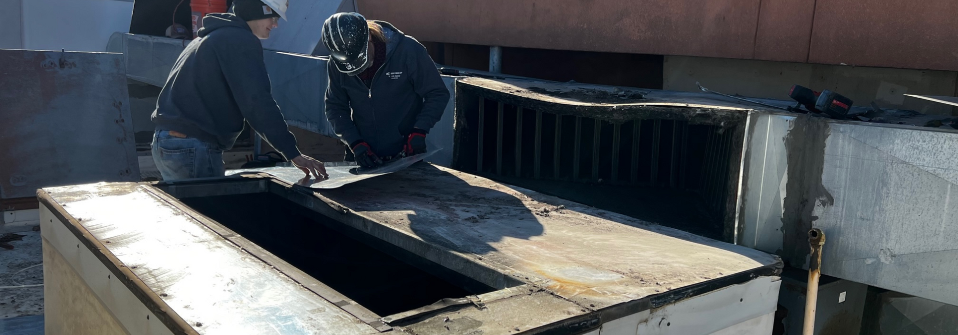 Workers inspecting a large rooftop tank or skylight under bright sunlight