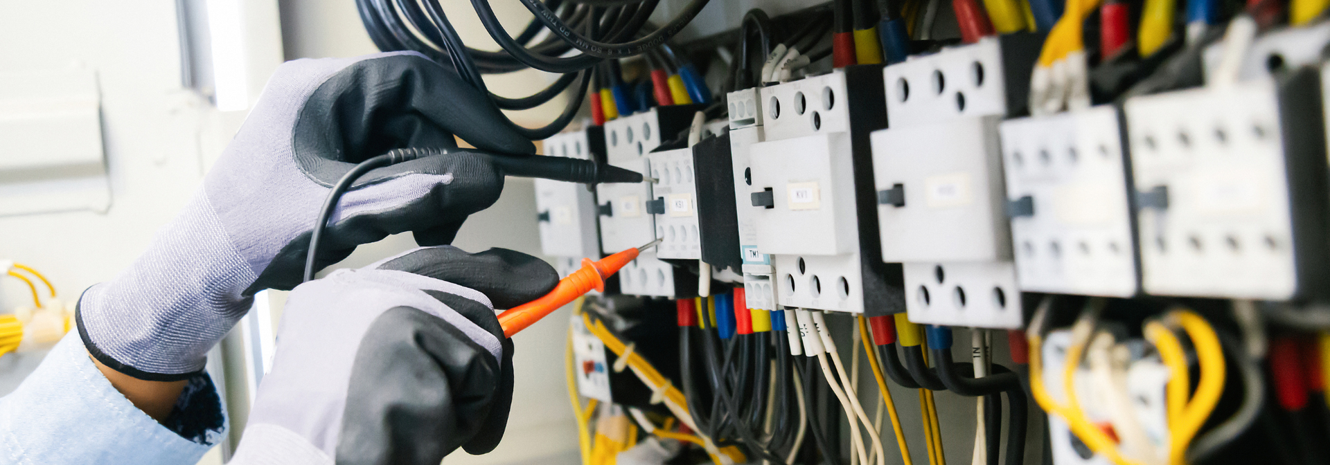 Gloved technician using pliers to work on an electrical control panel with wires and circuit breakers