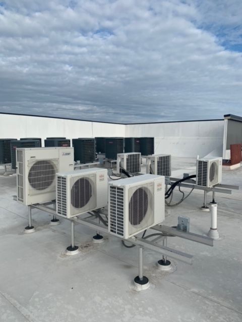 Rooftop HVAC units and ductless AC condensers on a flat roof under a cloudy sky.