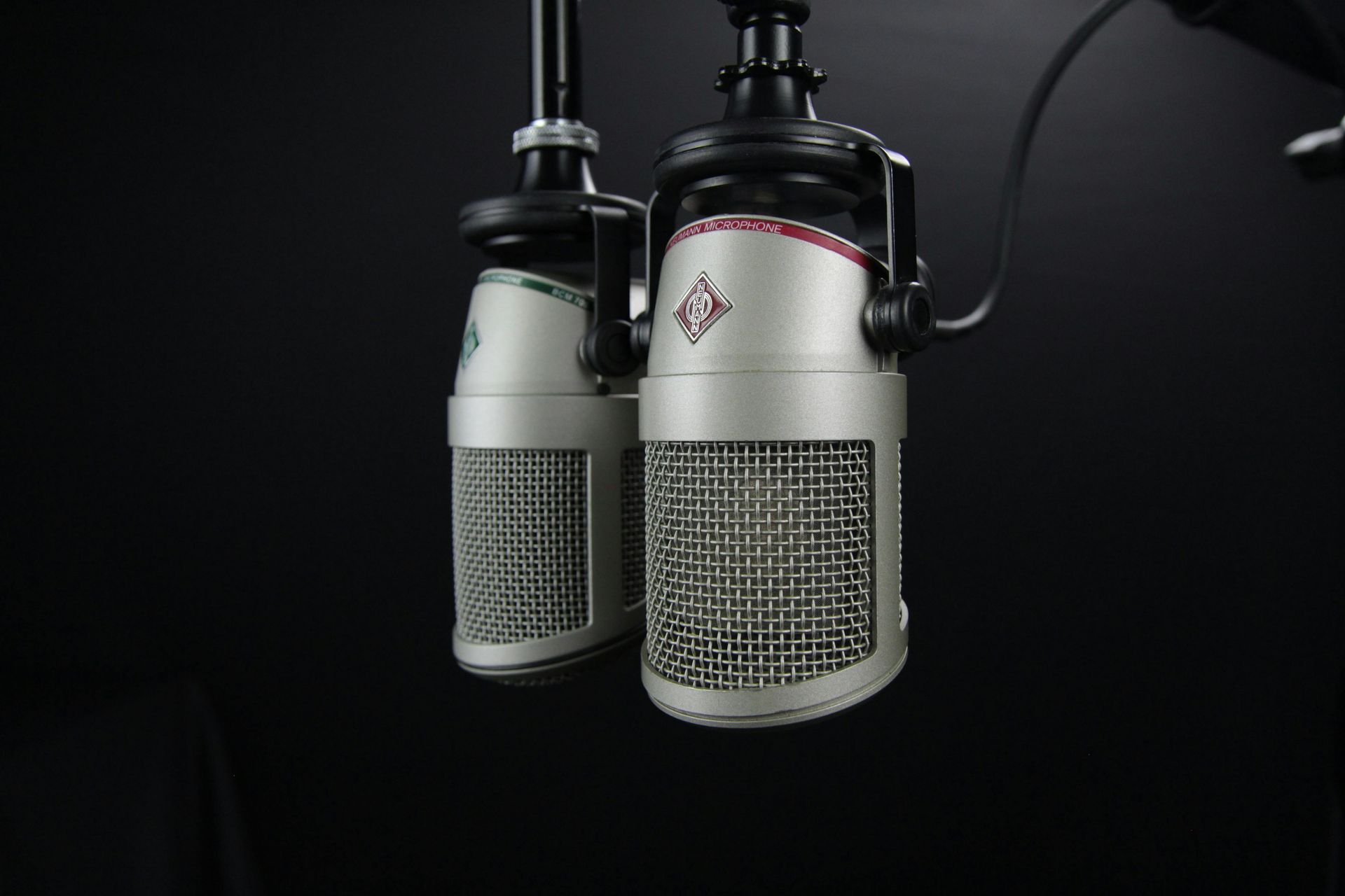 Two vintage silver microphones with red accents, hanging against a black background.