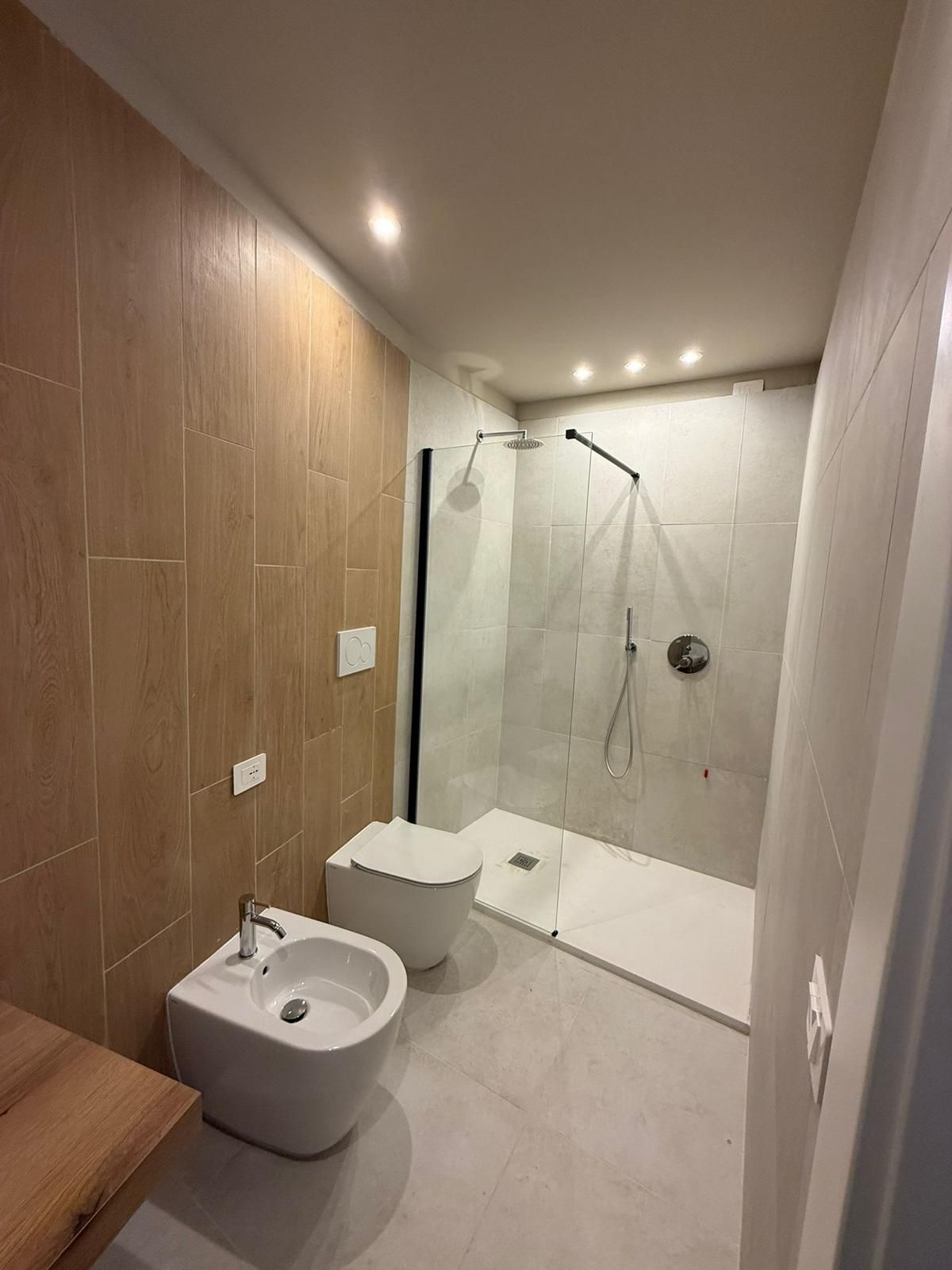 Bagno moderno con lavabo, WC e cabina doccia con finiture bianche e in legno.