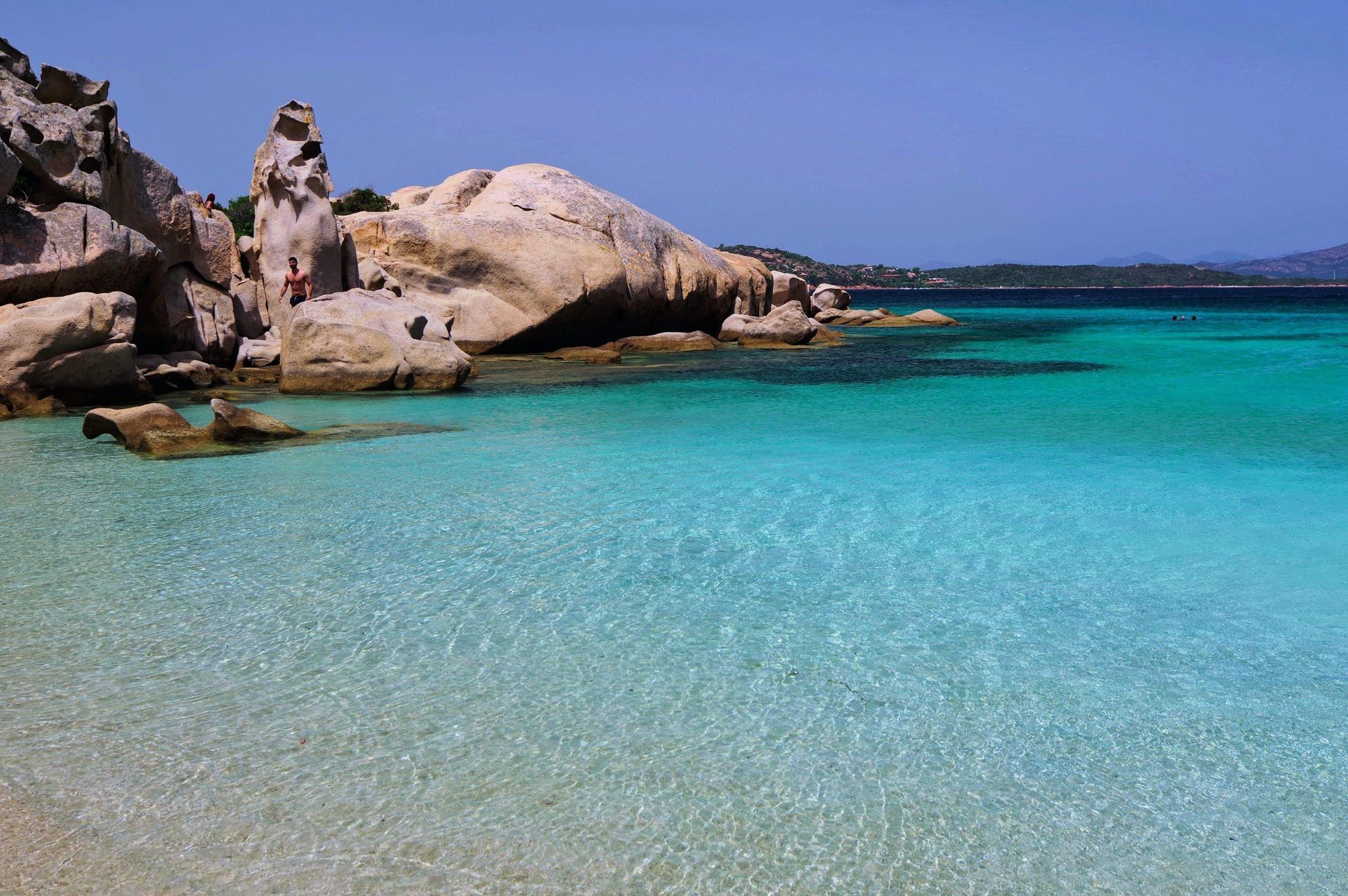 Oceano turchese accanto a una costa rocciosa sotto un cielo azzurro limpido.